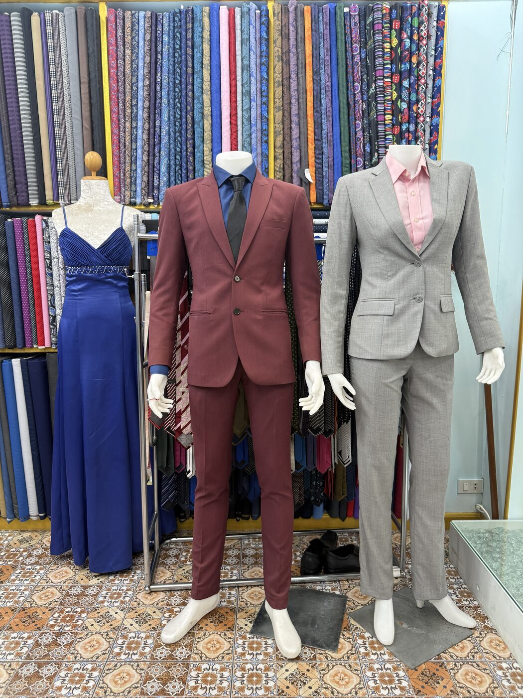 A burgundy men's suit and a light grey ladies' suit on mannequins in the shop