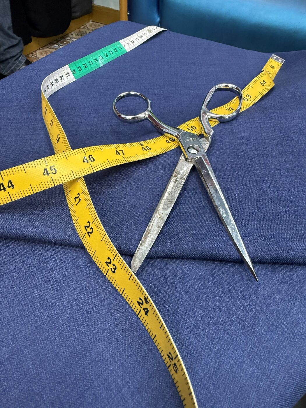 Tailor's shears and a measuring tape resting on navy suiting cloth