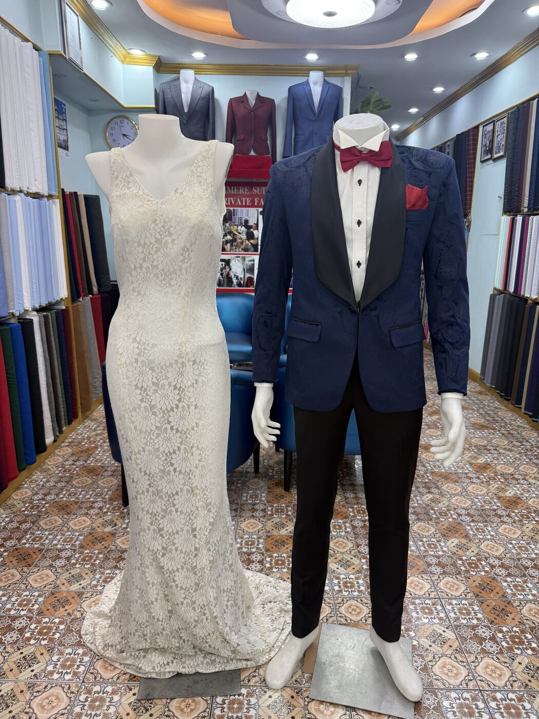 A white lace wedding dress and a navy paisley dinner jacket with bow tie, displayed side by side